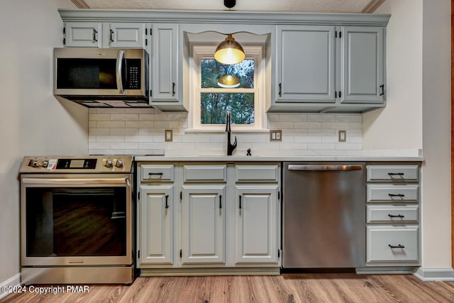 kitchen with light wood finished floors, gray cabinetry, a sink, appliances with stainless steel finishes, and light countertops