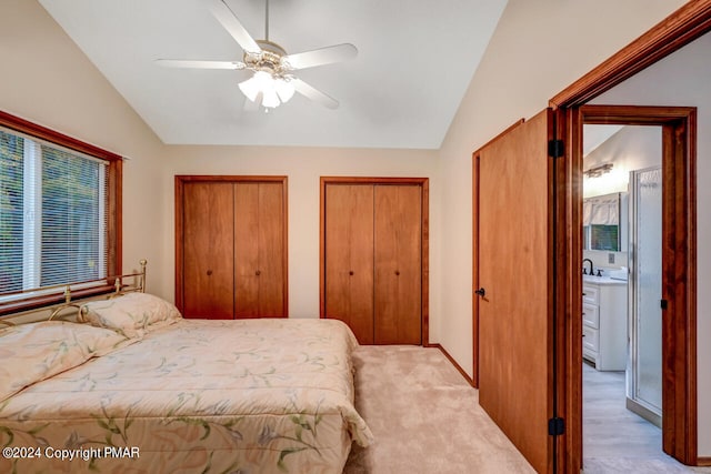 bedroom featuring a ceiling fan, vaulted ceiling, light colored carpet, and two closets