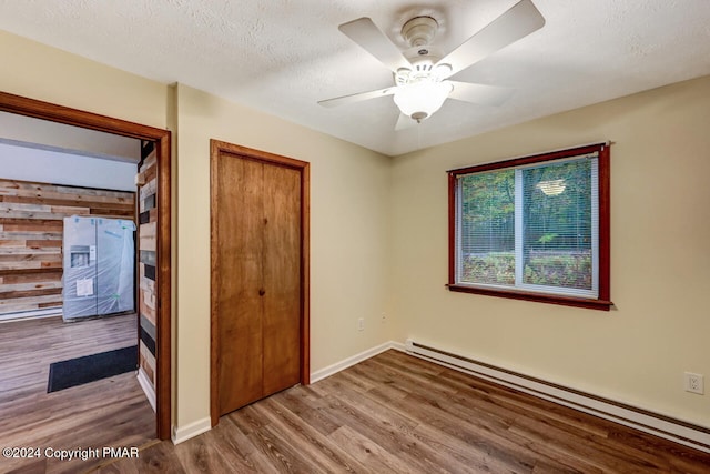 unfurnished bedroom with a textured ceiling, wood finished floors, a baseboard radiator, baseboards, and ceiling fan