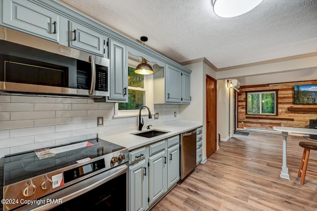 kitchen featuring light wood-type flooring, a sink, backsplash, appliances with stainless steel finishes, and light countertops