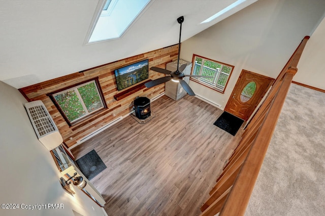 living room featuring wooden walls, ceiling fan, a skylight, wood finished floors, and high vaulted ceiling