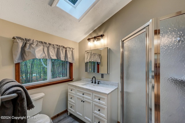 full bathroom featuring toilet, a textured ceiling, vaulted ceiling with skylight, a shower stall, and vanity