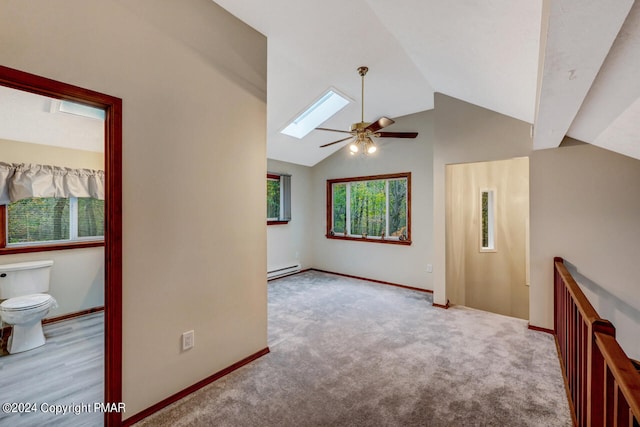 carpeted empty room featuring baseboards, vaulted ceiling with skylight, baseboard heating, and a ceiling fan