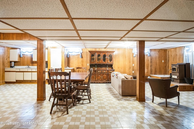 dining space featuring a drop ceiling, sink, wooden walls, and a wood stove