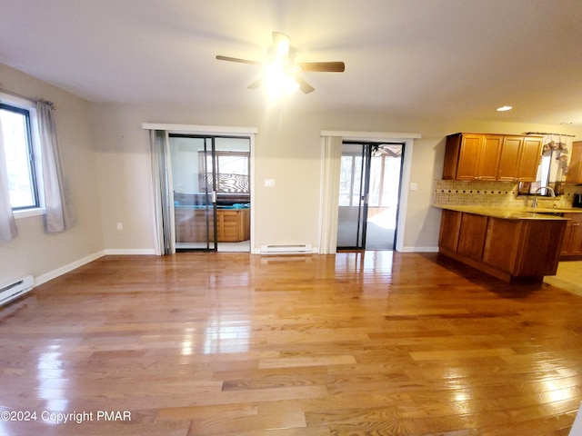 unfurnished living room featuring a baseboard heating unit, light wood-style floors, baseboards, and a ceiling fan