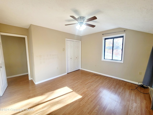 unfurnished bedroom with light wood finished floors, baseboards, lofted ceiling, a textured ceiling, and a closet