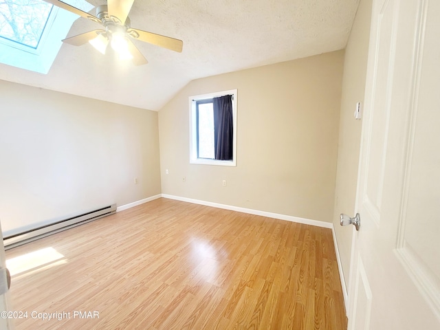 additional living space with lofted ceiling with skylight, light wood-type flooring, a textured ceiling, and baseboard heating