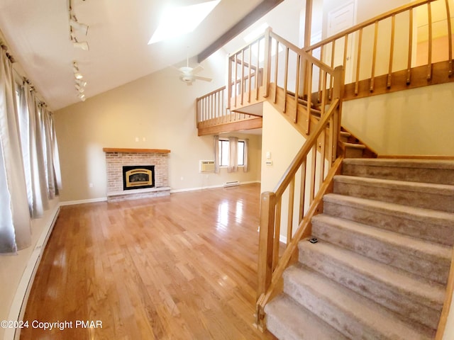 unfurnished living room featuring a skylight, stairway, rail lighting, light wood-type flooring, and a fireplace