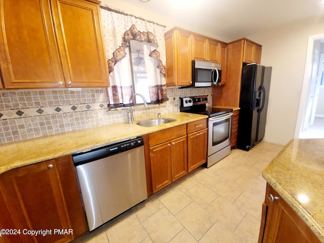 kitchen featuring stainless steel appliances, a sink, backsplash, and light stone countertops