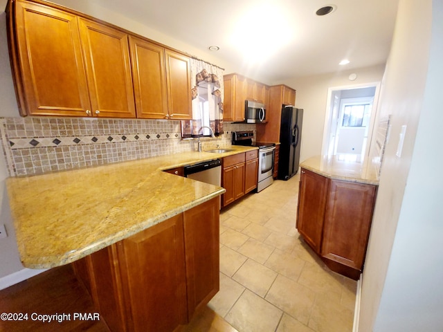 kitchen featuring stainless steel appliances, tasteful backsplash, a sink, light stone countertops, and a peninsula