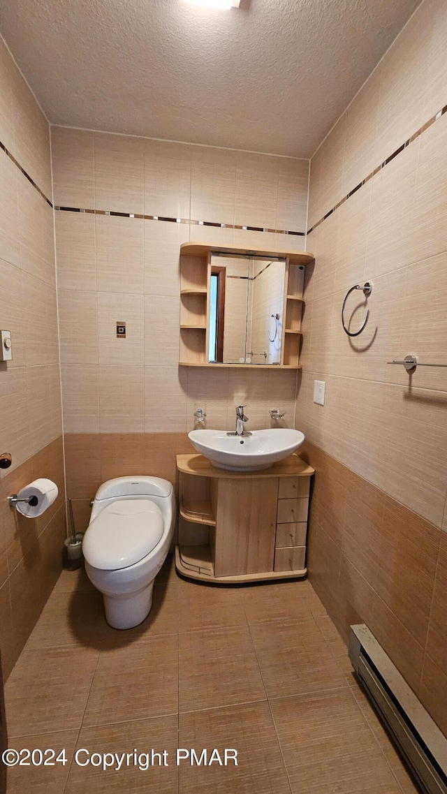 half bath featuring tile walls, toilet, baseboard heating, a textured ceiling, and vanity