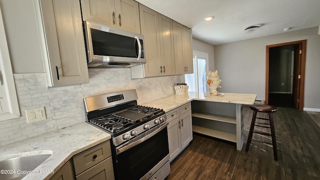 kitchen featuring stainless steel appliances, backsplash, dark wood-type flooring, light stone countertops, and a kitchen breakfast bar