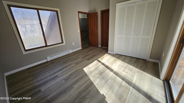 unfurnished bedroom with dark wood-style floors, a baseboard radiator, baseboards, and a closet