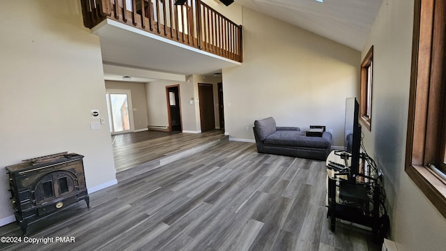 living room featuring a baseboard radiator, a high ceiling, baseboards, dark wood-style floors, and a wood stove