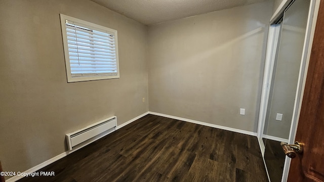 spare room featuring dark wood-style floors, baseboard heating, a textured ceiling, and baseboards