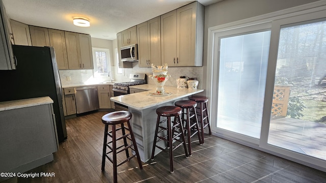 kitchen with dark wood finished floors, decorative backsplash, a breakfast bar area, a peninsula, and stainless steel appliances