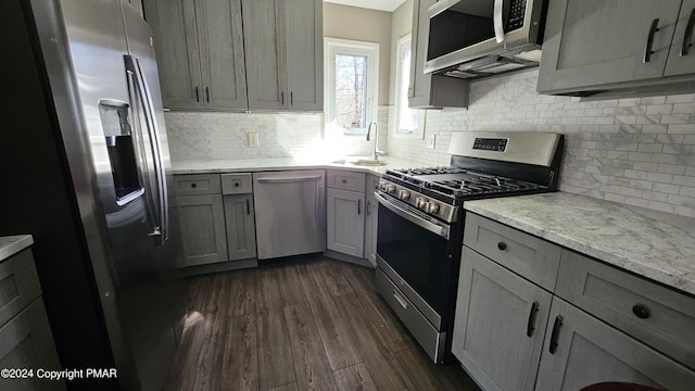 kitchen with dark wood-style floors, light stone countertops, gray cabinets, stainless steel appliances, and a sink