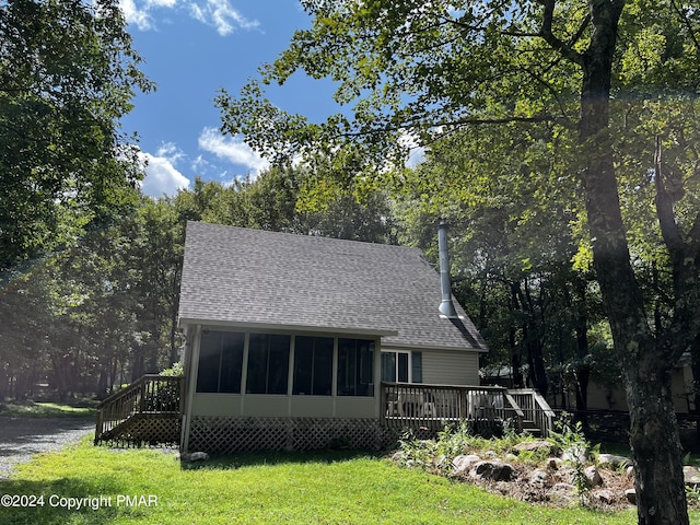 back of house with a shingled roof, a sunroom, a deck, a yard, and a wooded view