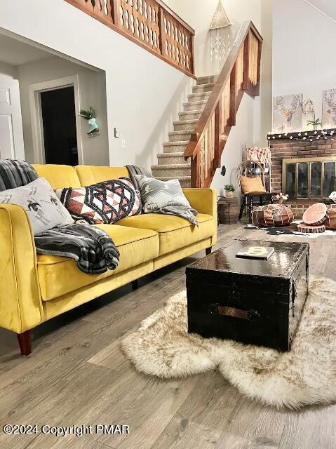 living area with a towering ceiling, stairs, a fireplace, and wood finished floors