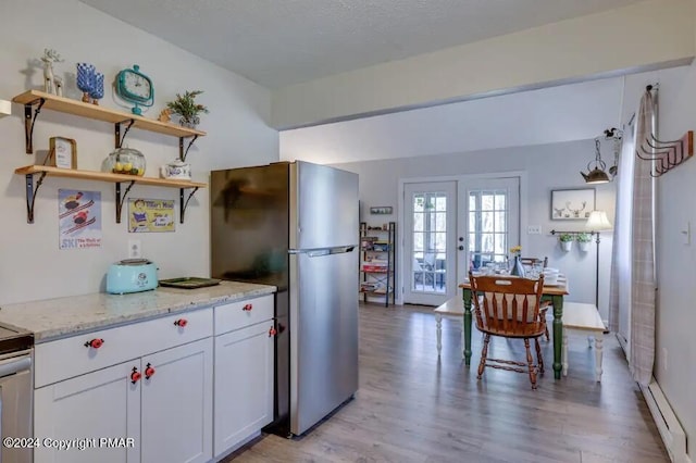 kitchen with light stone counters, freestanding refrigerator, french doors, light wood-type flooring, and white cabinetry