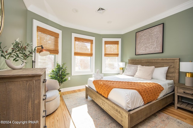 bedroom with light wood-type flooring, baseboards, visible vents, and crown molding