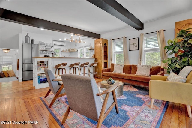 living area featuring a wall unit AC, an inviting chandelier, light wood finished floors, and beamed ceiling