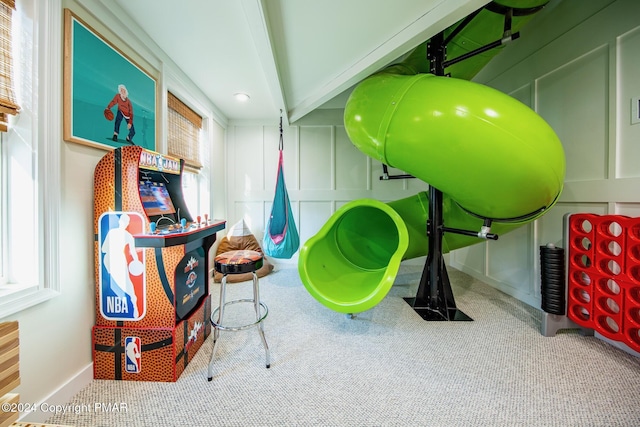 playroom with beamed ceiling, carpet, and a decorative wall