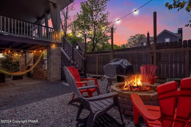 patio terrace at dusk featuring an outdoor fire pit, stairway, grilling area, and fence