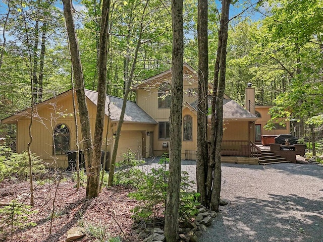 171 Flintlock Trl, Pocono Pines, PA 18350 - view of front of property featuring a shingled roof, an attached garage, gravel driveway, a wooden deck, and a chimney