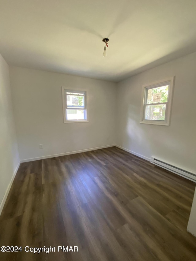 empty room with a baseboard heating unit, dark wood-style flooring, and baseboards