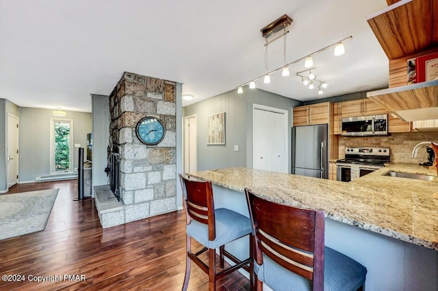 kitchen with dark wood finished floors, appliances with stainless steel finishes, a peninsula, light stone countertops, and a sink