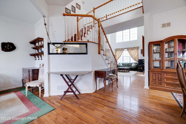 interior space with hardwood / wood-style flooring, a high ceiling, visible vents, stairs, and crown molding