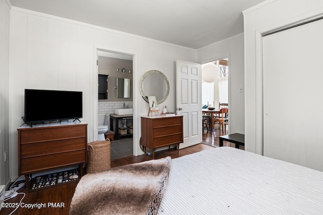 bedroom featuring a closet, dark wood-type flooring, ornamental molding, connected bathroom, and a sink