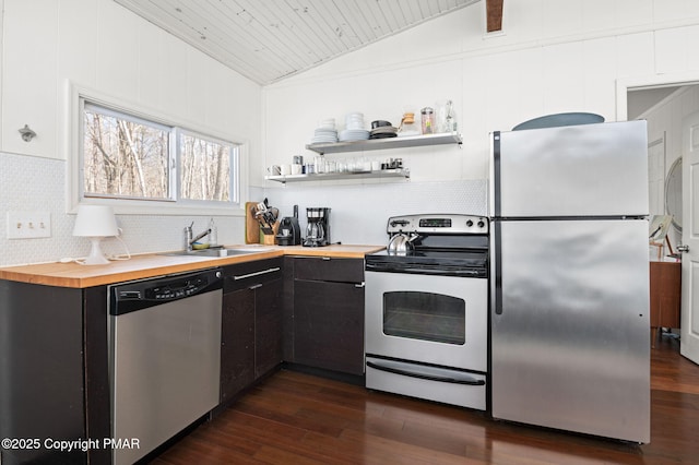 kitchen with butcher block countertops, appliances with stainless steel finishes, dark wood-type flooring, vaulted ceiling, and a sink