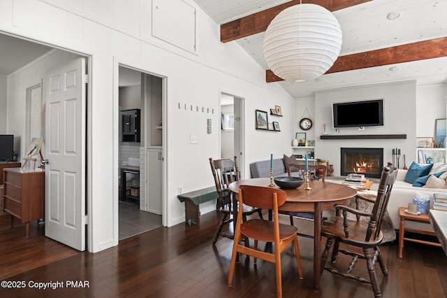 dining space with vaulted ceiling with beams, dark wood-type flooring, and a glass covered fireplace