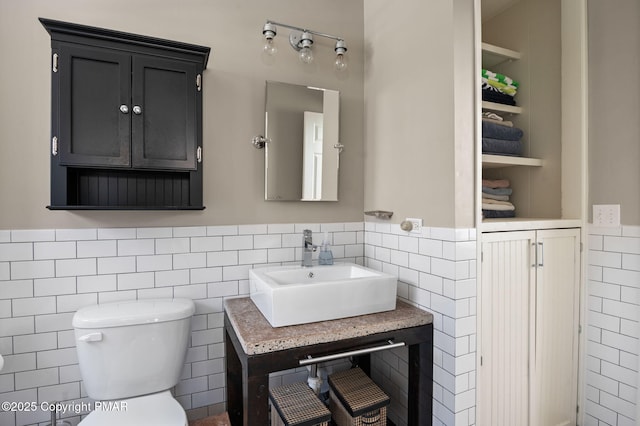 bathroom with toilet, built in shelves, tile walls, and a sink