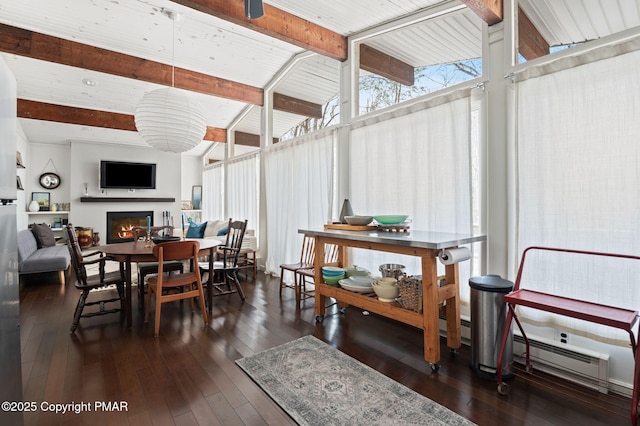 dining space featuring dark wood-style floors, lofted ceiling with beams, baseboard heating, a glass covered fireplace, and a wall of windows