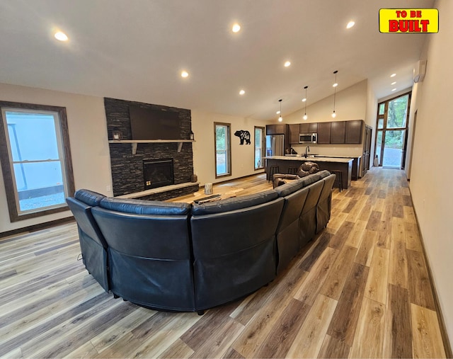 living room with light wood finished floors, a stone fireplace, recessed lighting, and vaulted ceiling