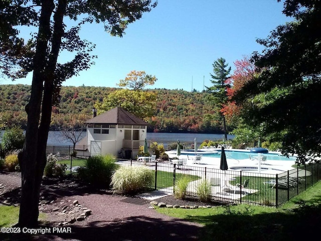 pool with a water view, a forest view, a patio area, and fence