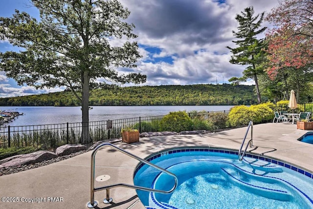 view of pool with a community hot tub, a water view, fence, and a forest view