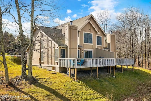 back of house featuring a deck, roof with shingles, a lawn, and board and batten siding