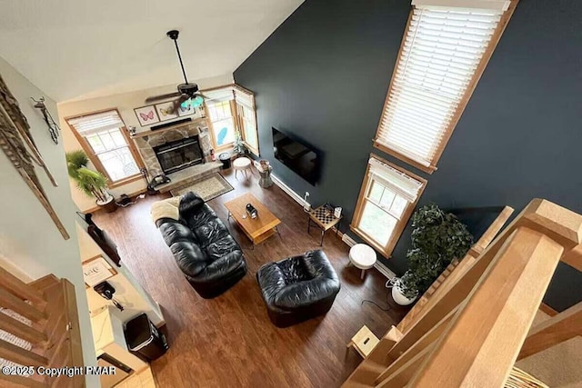 living area with baseboards, a ceiling fan, lofted ceiling, wood finished floors, and a stone fireplace