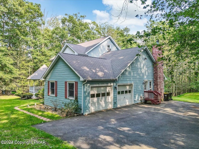 view of home's exterior with a shingled roof, a lawn, a chimney, aphalt driveway, and an attached garage