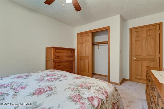 bedroom featuring baseboards, a ceiling fan, light colored carpet, a textured ceiling, and a closet