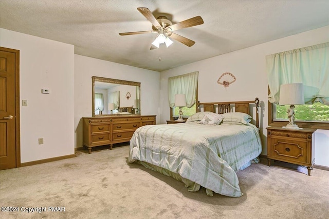 bedroom featuring a ceiling fan, light carpet, a textured ceiling, and baseboards