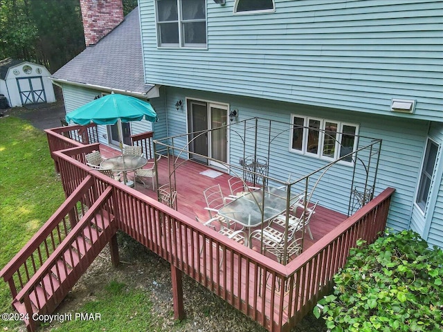 deck with a yard, a storage unit, outdoor dining space, an outdoor structure, and stairs