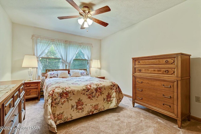 bedroom with light carpet, a textured ceiling, a ceiling fan, and baseboards