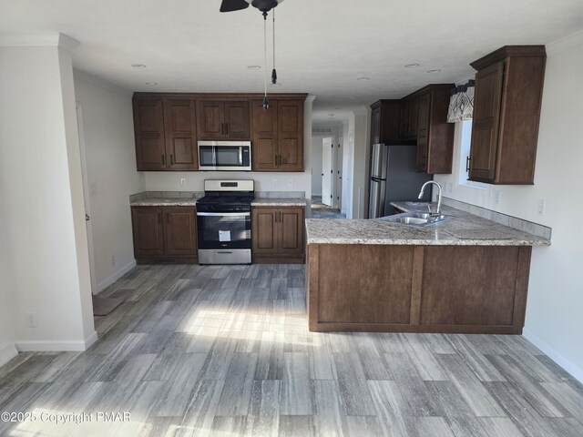 kitchen with baseboards, a peninsula, a sink, appliances with stainless steel finishes, and light wood-type flooring