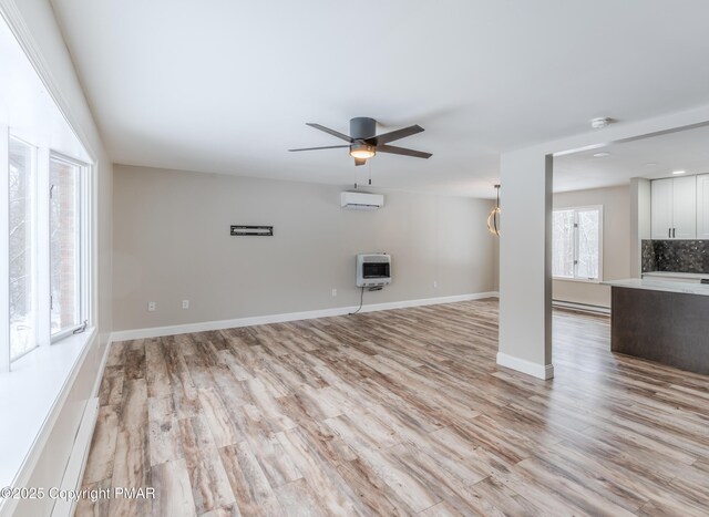 unfurnished living room with heating unit, an AC wall unit, light hardwood / wood-style flooring, and ceiling fan