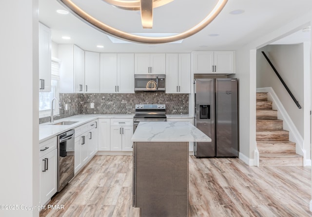 kitchen featuring a center island, white cabinetry, sink, stainless steel appliances, and light stone counters